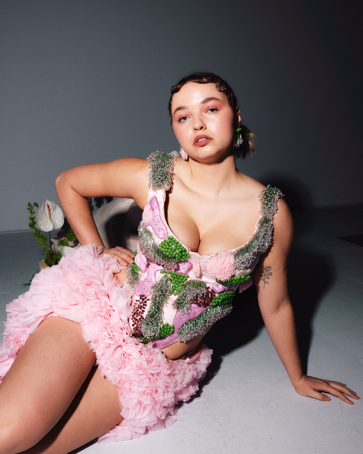 Emma Van Engelen, founder and designer of Bhumi, modeling the Graduation Beaded Corset in pink and green. The corset, featured on the front cover of Elle Netherlands and worn by Bridgerton star Nicola Couglan, is showcased as Emma sits on the floor, facing the camera, embodying Bhumi's design ethos of bold, sustainable luxury fashion.