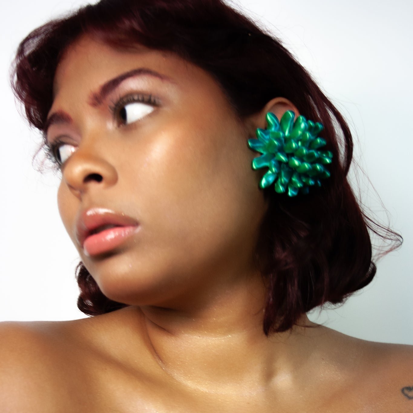 A headshot of a muse adorned with the Anemone earcuff in satin blue/green multitone from Bhumi's debut collection 'Bathe in the Waters.' The coral-inspired 3D-printed accessory gleams in vibrant hues, complementing the muse's ethereal style.