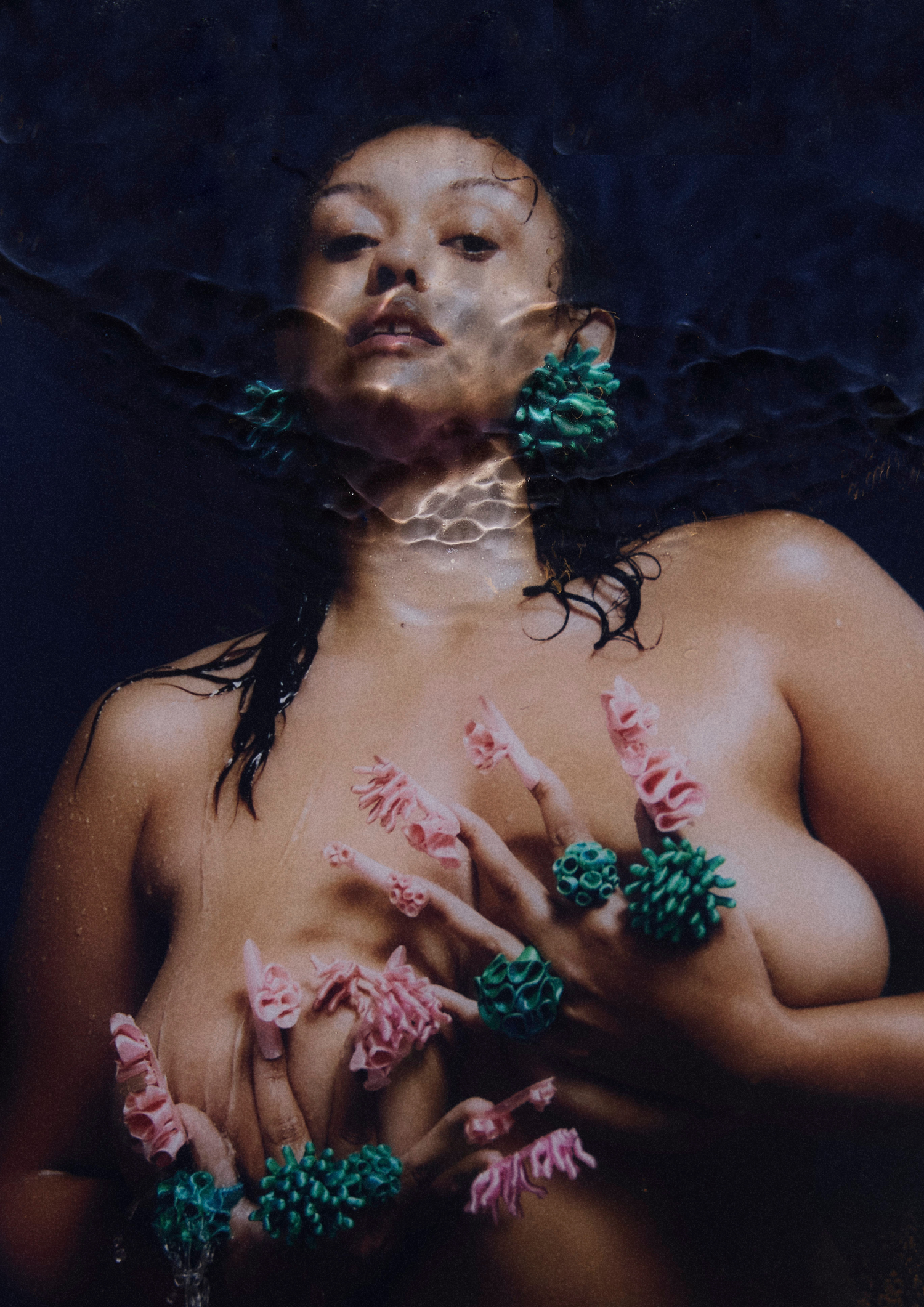 Model wearing Bhumi Clothing's 'Bathe in the Waters' collection, featuring coral-inspired 3D-printed Spheara and Marina rings in Satin Blue/Green Multitone, Anemone earrings, and an ear cuff. The model, with satin pink nails, holds her chest in a front-facing pose, showcasing the intricate design of the sustainable luxury jewelry.