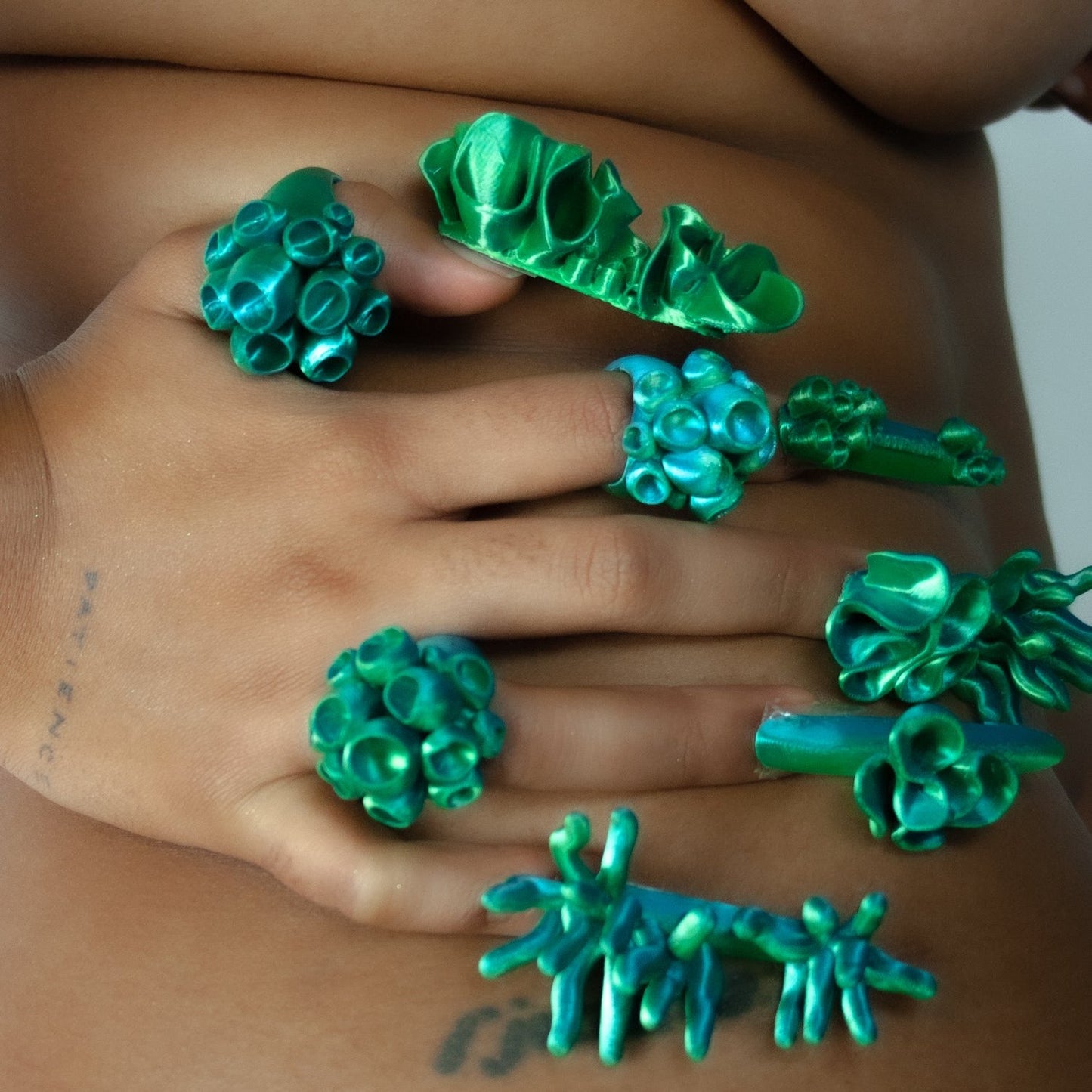 A close-up shot of a hand against rolls on the body, wearing the Spheara rings in green from Bhumi's 'Bathe in the Waters' collection. The bold 3D-printed rings stand out with their organic, textured design, reflecting the coral-inspired aesthetic.