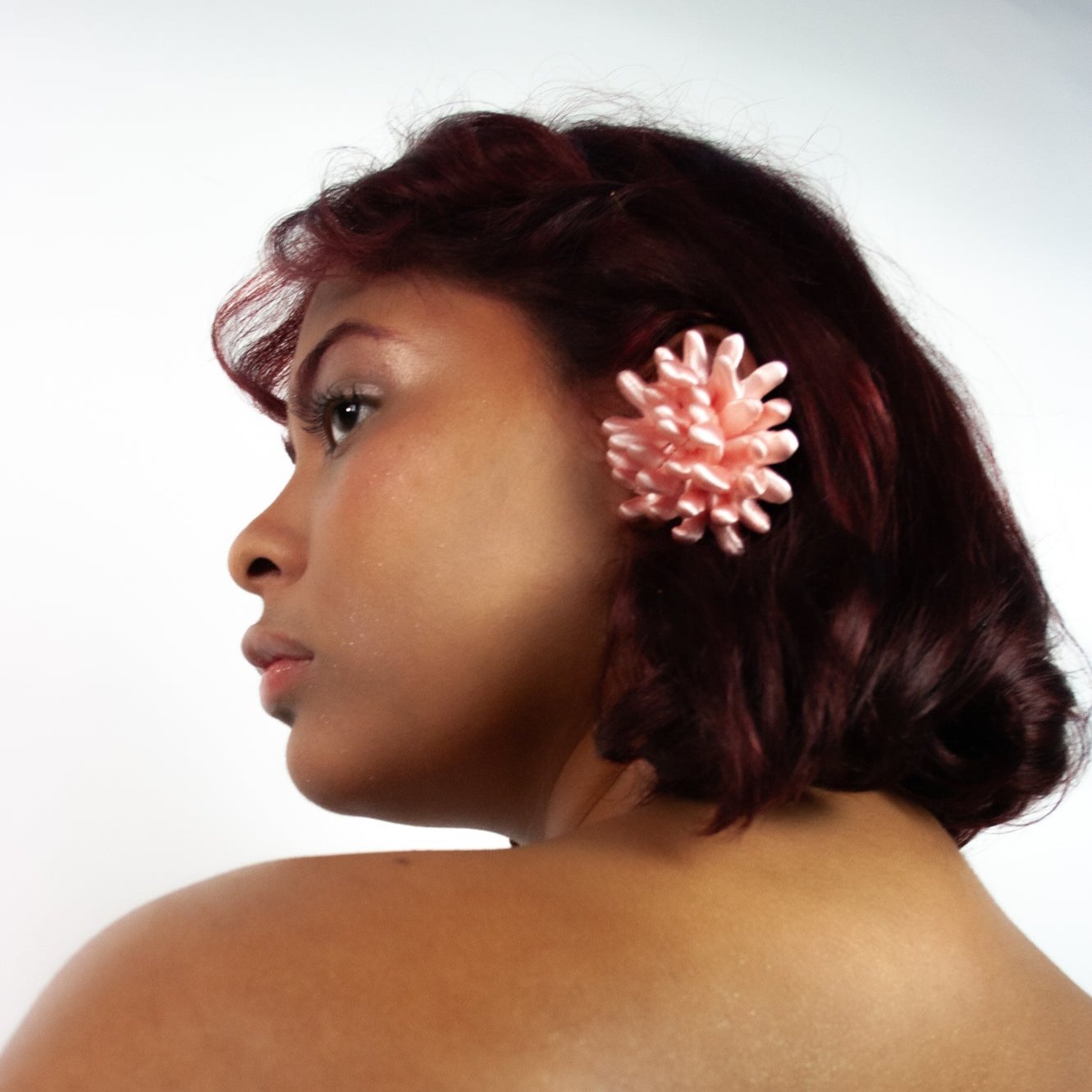 A headshot of a muse wearing the Anemone earcuff in satin baby pink from Bhumi's debut collection 'Bathe in the Waters.' The coral-inspired 3D-printed accessory catches the light, showcasing its intricate design and bold texture.
